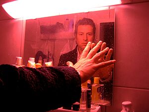 Salwski berührt mit seiner Hand sein Spiegelbild in einem rot beleuchteten Raum