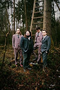 Vier Musiker vor einer Holzleiter im Wald