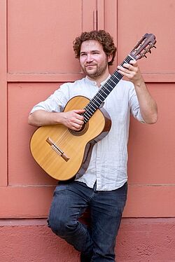 Gitarrist Adrian Ingerl mit Gitarre im Arm vor roter Tür