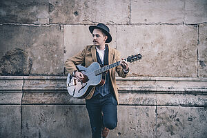 Jonathan Gordon vor Steinwand mit Gitarre