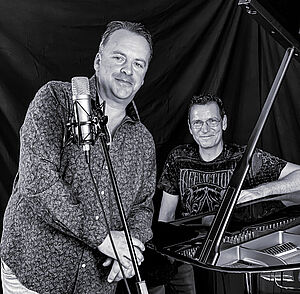 Georg Kleesattel und Martin Stellmacher neben Piano in graustufen