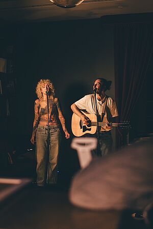 Eine Frau und ein Mann mit einer Gitarre in einem dunklen Raum